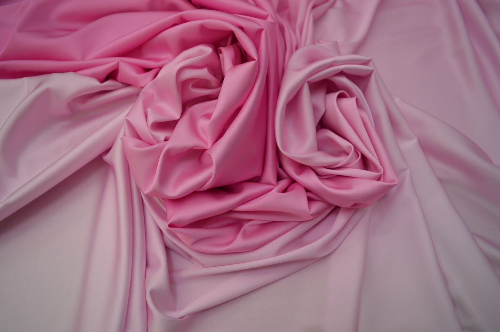 Close-up of pink satin fabric intricately folded, showing its smooth glossy sheen