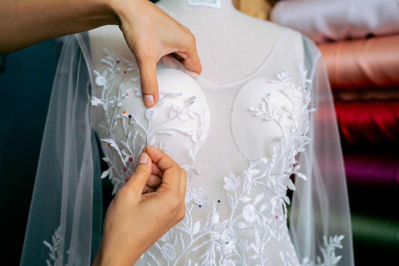Hands pinning lace and satin fabric onto a dress form for a bridal gown
