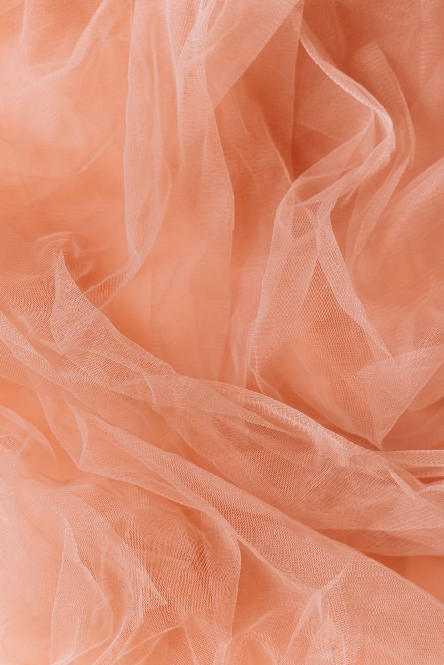 Sheer orange fabric draped in soft folds, showing its light, translucent quality