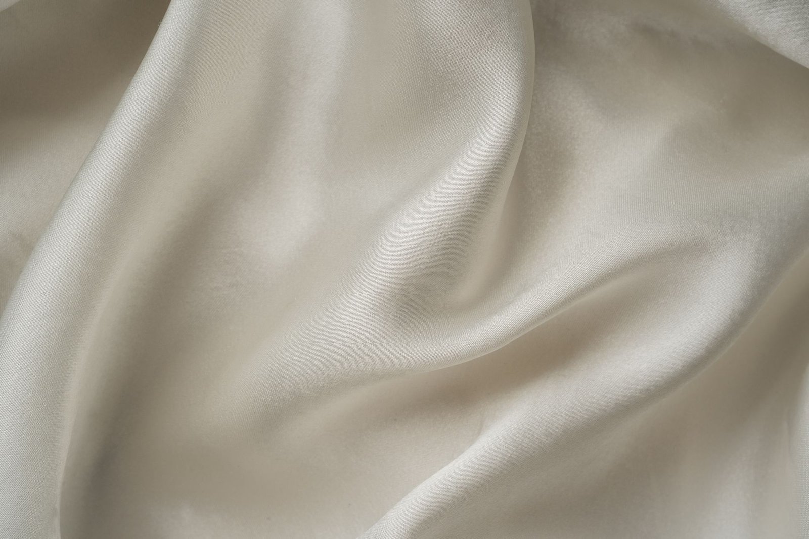 Flowing ivory charmeuse satin fabric with soft folds and sheen