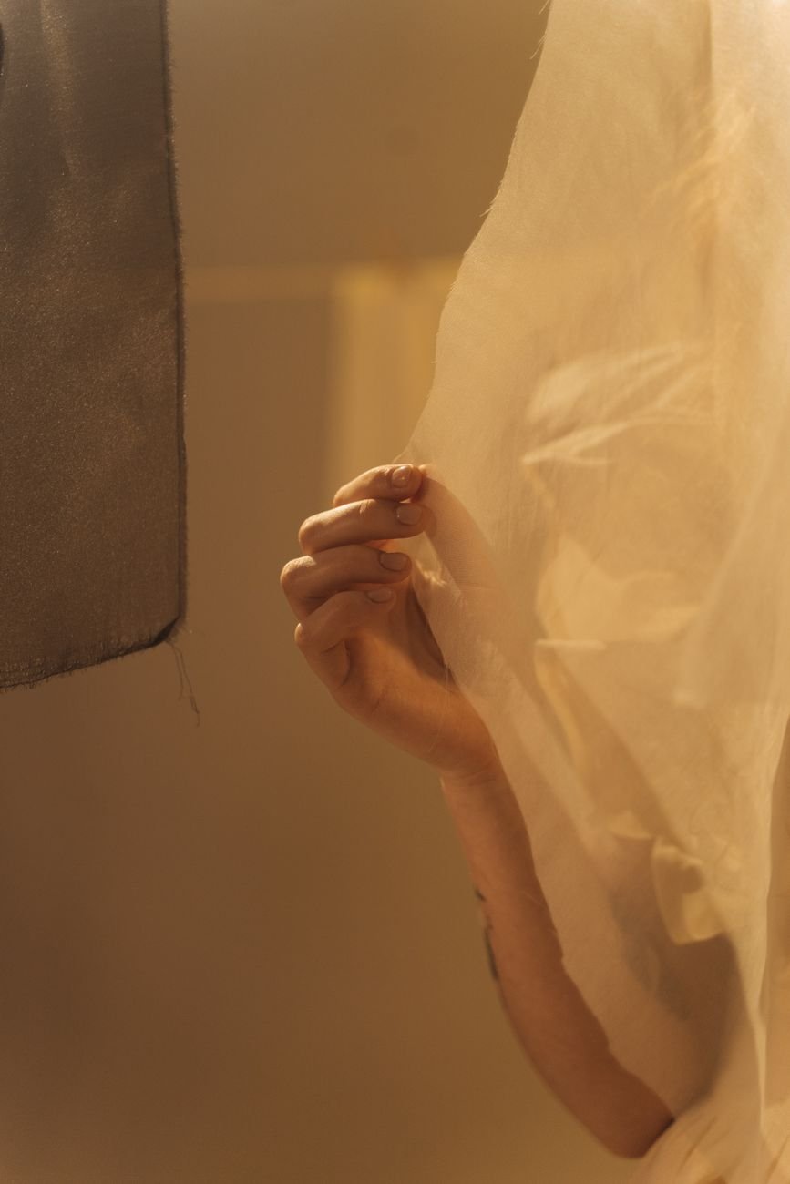 A hand holding a length of sheer fabric up toward a light source to check the weave