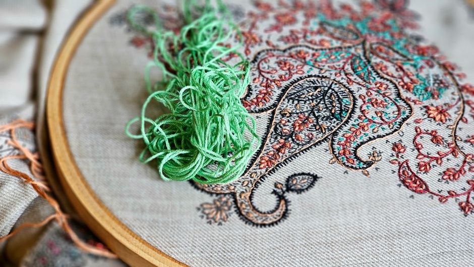 Close-up of a hand stitching colorful thread through fabric held in an embroidery hoop