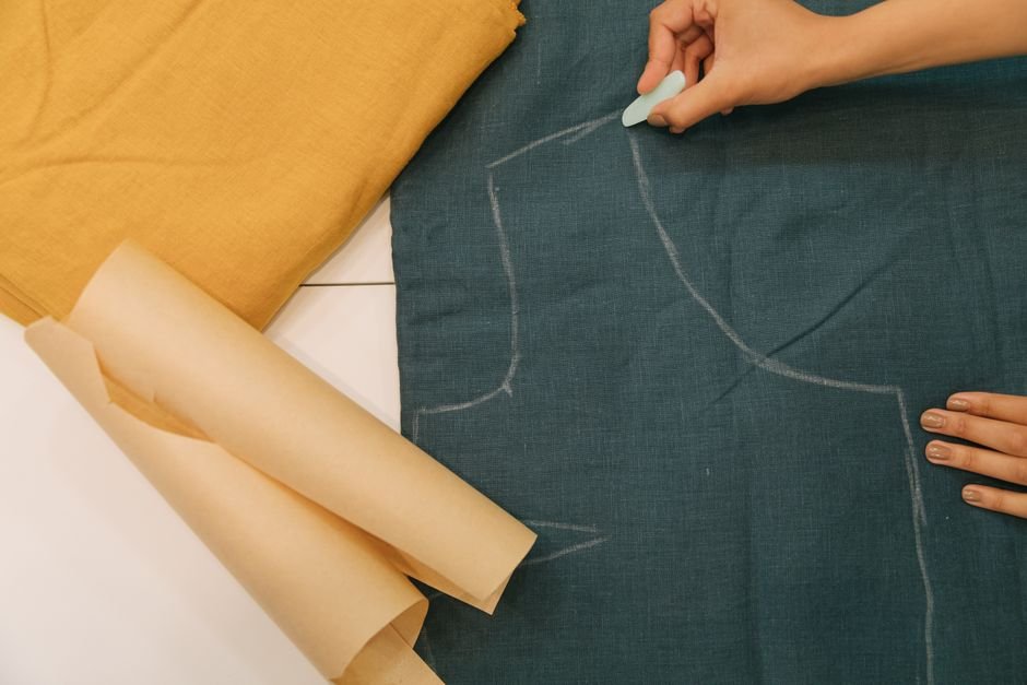 Hand marking a garment pattern outline onto dark fabric with fabric chalk