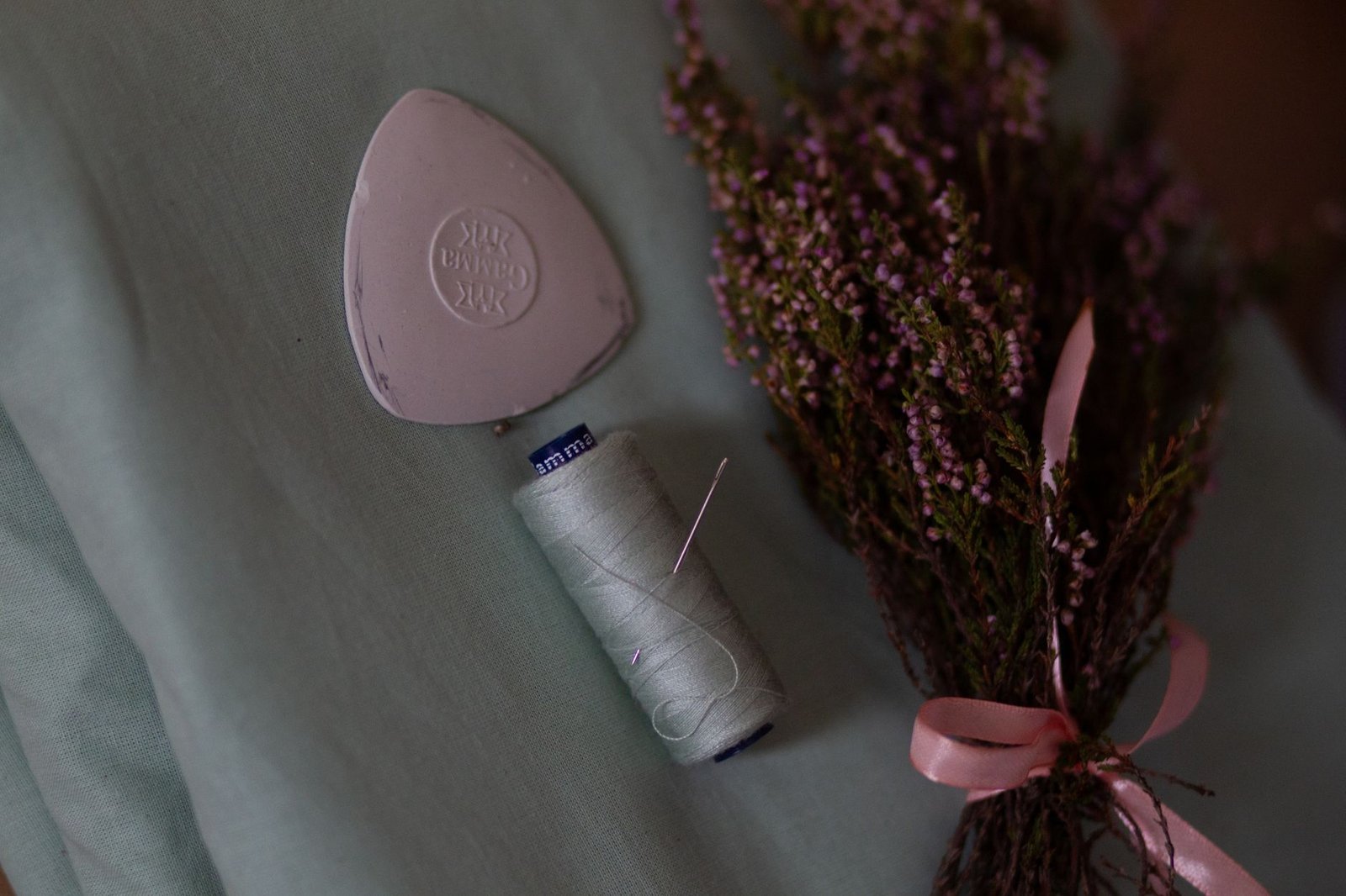 Sewing thread, needle, and a chalk marker pouch beside dried flowers