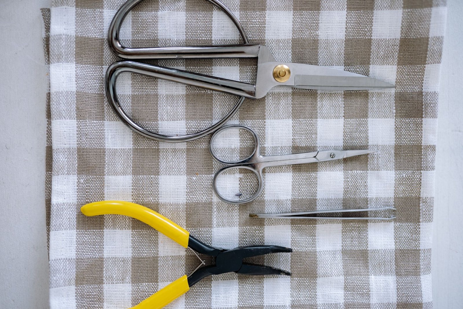 Sewing shears, small scissors, thread, and buttons arranged on gingham fabric
