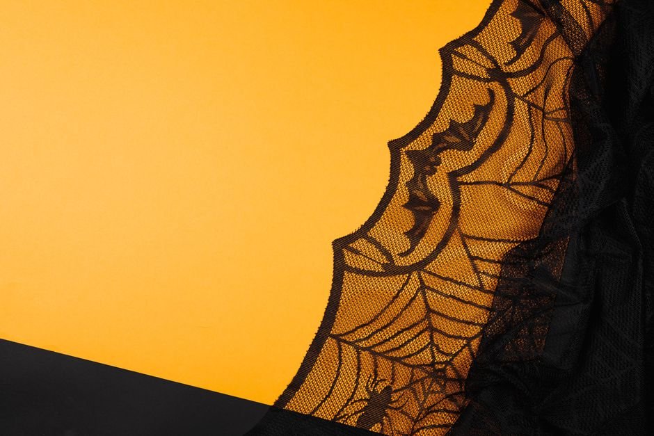 Black lace spiderweb pattern fabric detail on an orange background for Halloween sewing