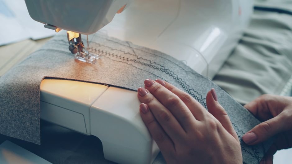 Hands guiding gray fabric under a sewing machine needle while stitching