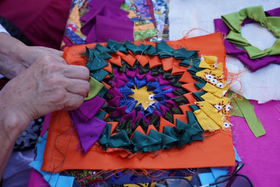 Hands folding fabric triangles into a coiled rosette pattern similar to jelly roll rug construction