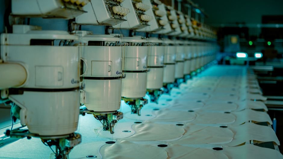 Row of industrial embroidery machine heads stitching fabric panels