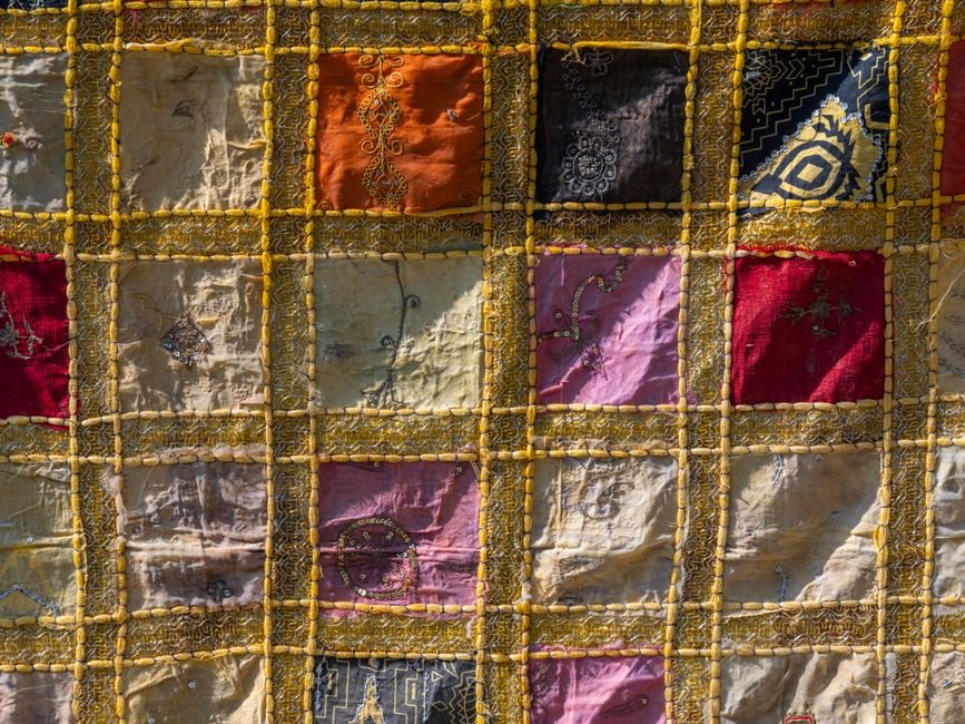 Patchwork textile with a grid of fabric squares bordered in trim, illustrating a pieced square layout