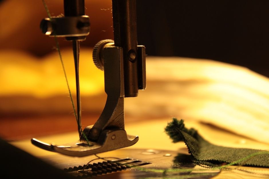 Sewing machine presser foot stitching green thread into folded fabric