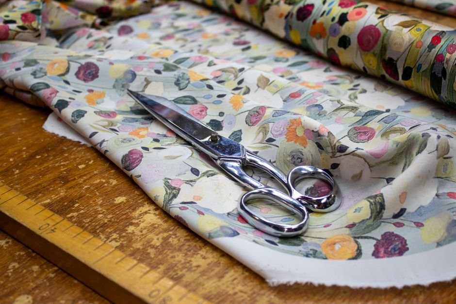 Scissors resting on a floral printed cotton fabric beside a wooden ruler