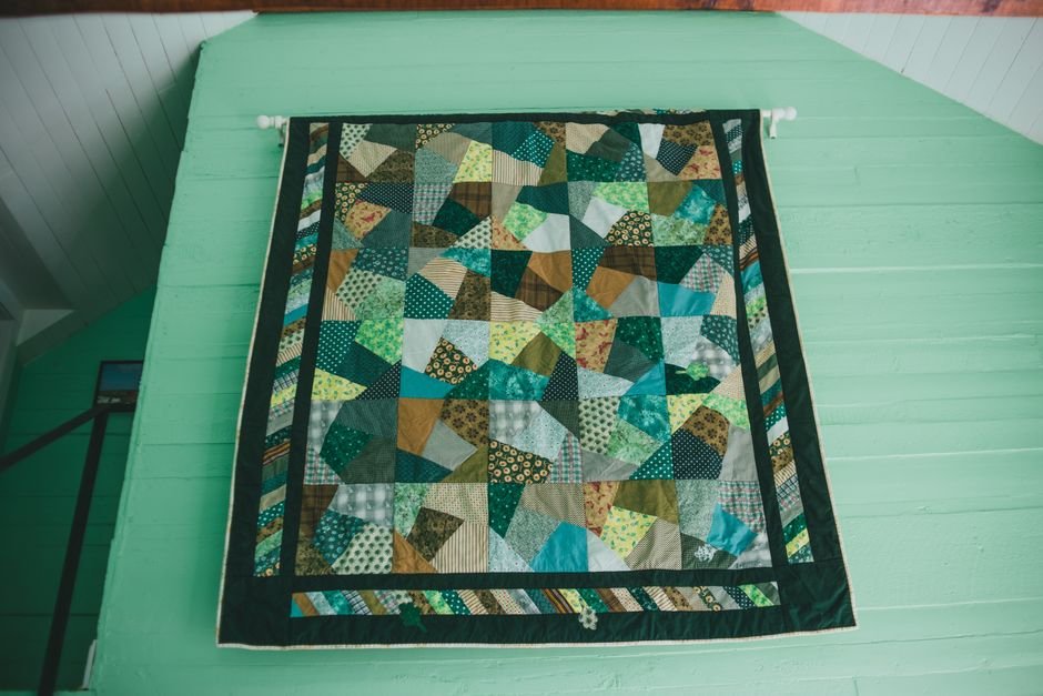Finished green and gold patchwork quilt hanging on display