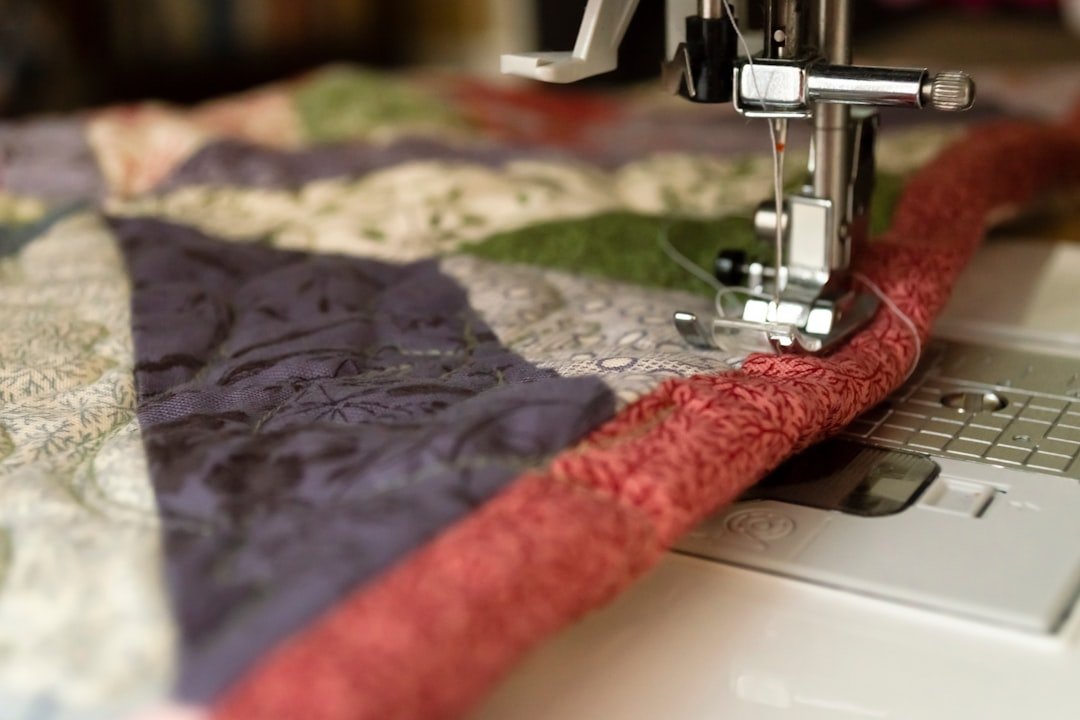 Sewing machine stitching red binding onto a finished patchwork quilt