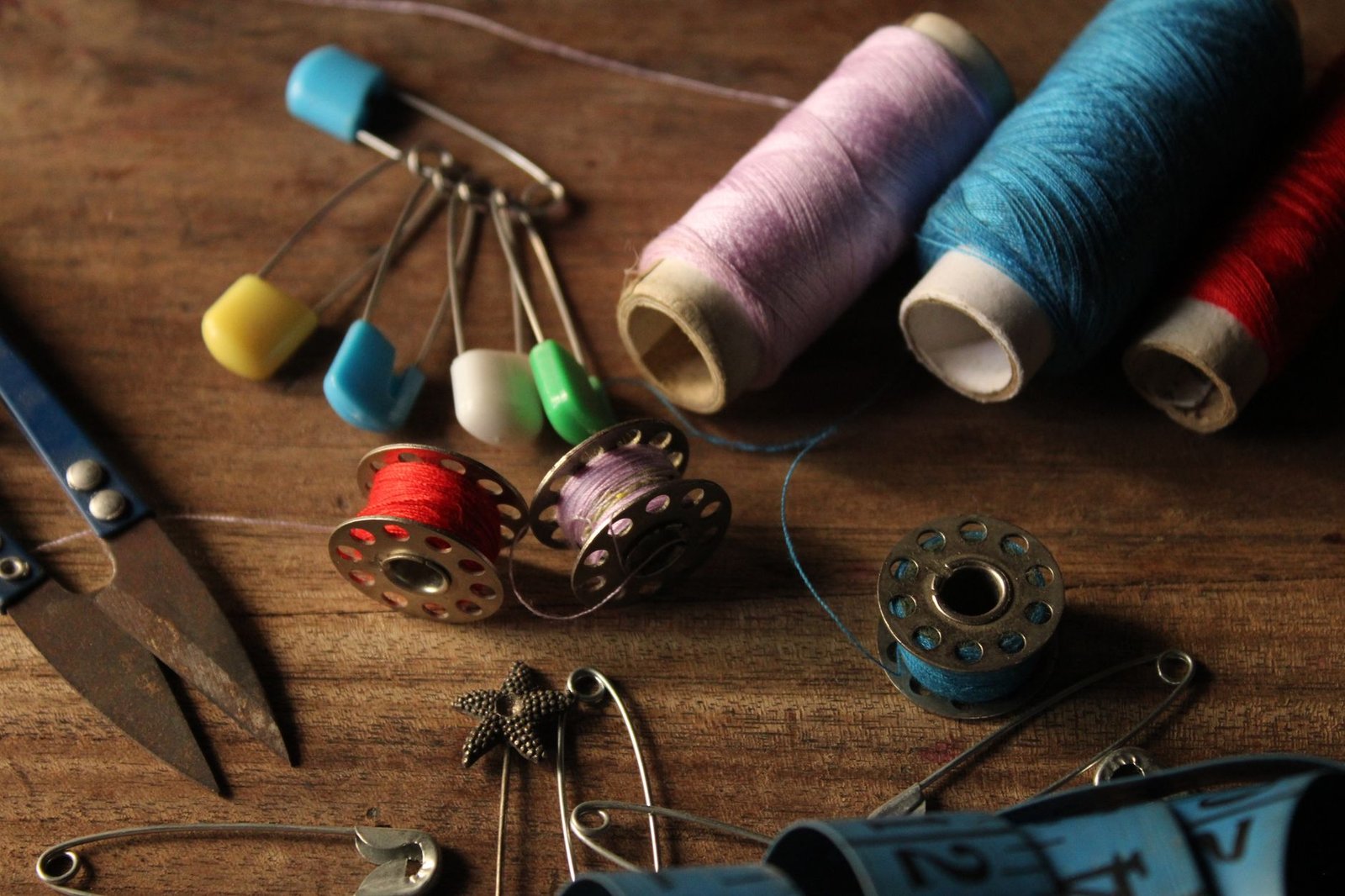 Safety pins, thread spools, and bobbins arranged on a wooden table