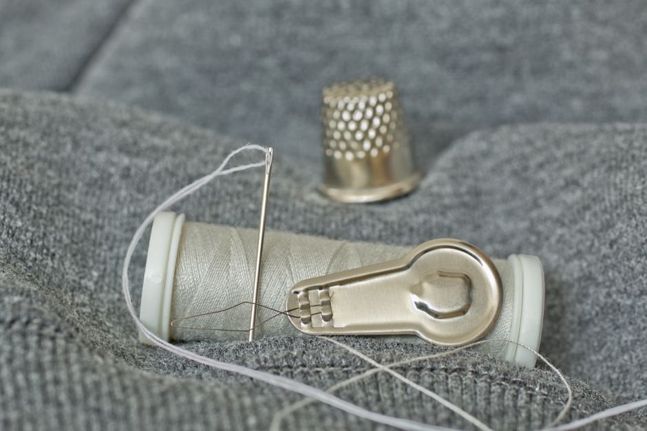 Sewing thimble, needle, and thread spool resting on gray quilted fabric