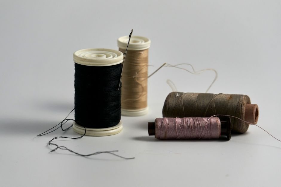 Fine thread spool beside a sewing needle showing the thin profile of silk thread