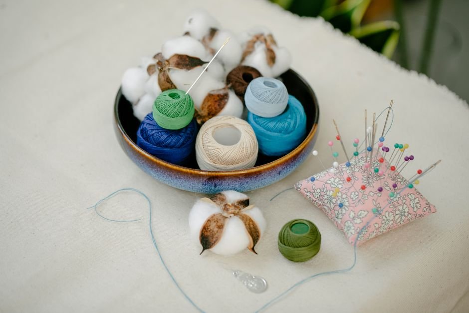 Bowl of thread and cotton bolls beside a pin cushion full of straight pins