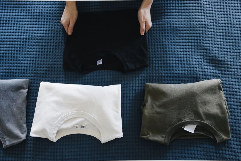 Folded plain t-shirts in black, white, and olive arranged in a row