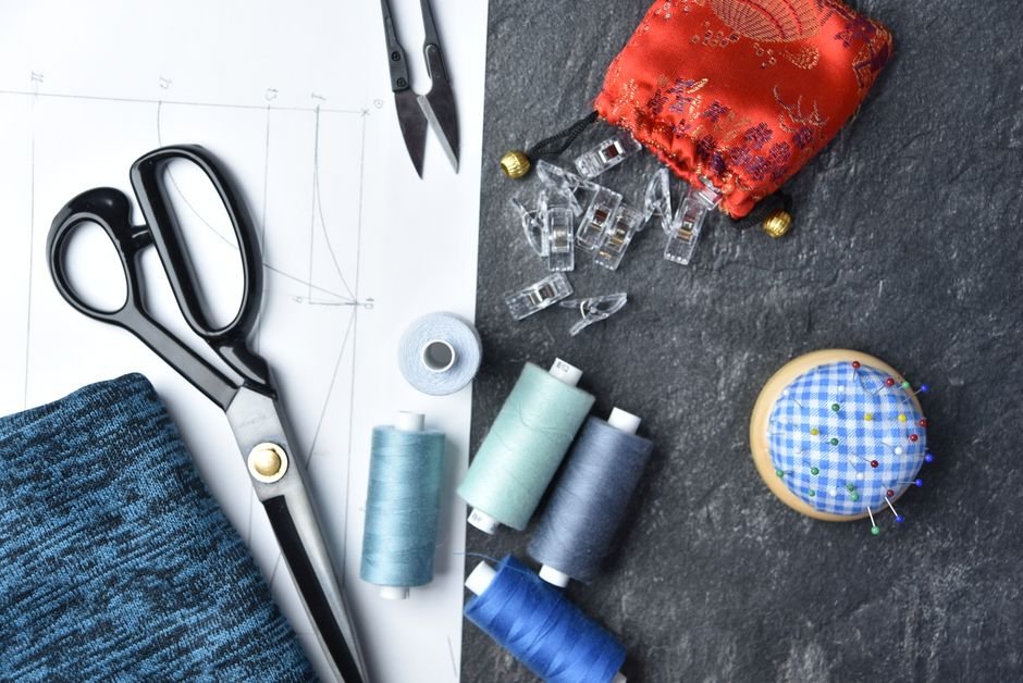 Sewing notions flat lay with scissors, thread spools, clips, and a pincushion
