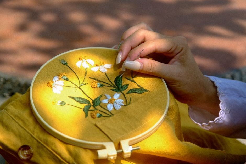Hand working a satin stitch in an embroidery hoop showing smooth fill stitching