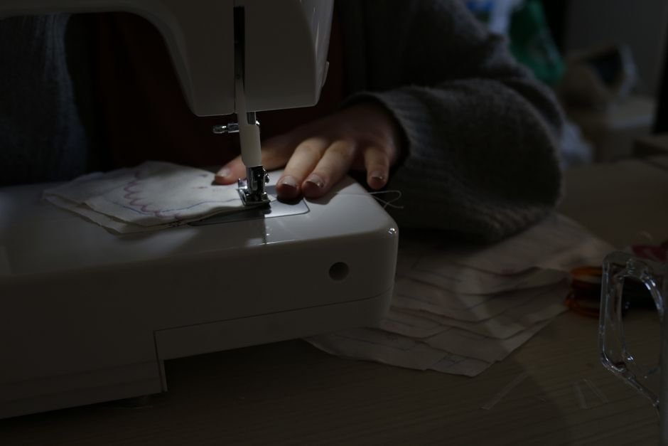 Hands guiding fabric under a sewing machine needle in dim light